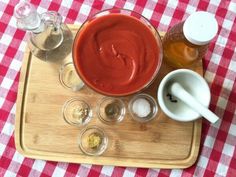 a wooden tray topped with cups and sauces on top of a checkered table cloth