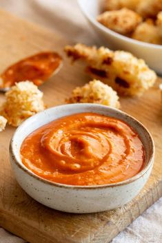 a bowl of sauce sitting on top of a wooden cutting board next to other foods