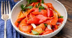 a white bowl filled with sliced tomatoes and parsley on top of a wooden table