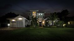 a house with lights on in the front yard and palm trees around it at night