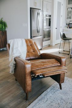 a brown leather chair sitting in front of a refrigerator freezer next to a rug