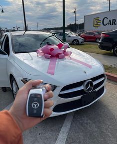 a person holding a cell phone in front of a car with a bow on it