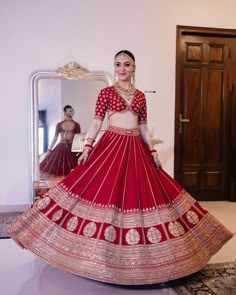 a woman in a red and gold lehenga is standing near a mirror with her reflection