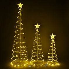 three lighted christmas trees in the dark with stars on top and one standing up against it's sides