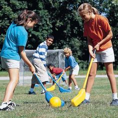 three children are playing with plastic balls and paddles on the grass in a park