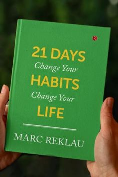 a person holding up a green book with the title 21 days change your habitts change your life