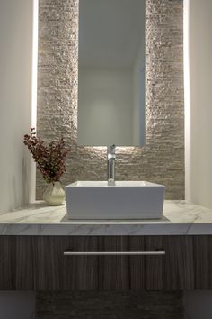 a bathroom sink sitting under a mirror next to a vase with flowers in front of it