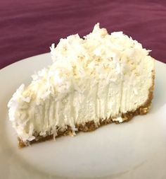 a slice of coconut cream pie on a white plate with purple cloth in the background