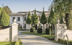 a large white house with lots of trees and bushes on the front yard, along with two driveways