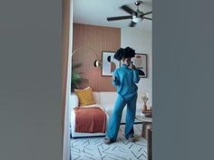 a woman in blue jumpsuits is standing in the living room with a ceiling fan