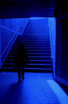 a person is walking up some stairs in the dark with blue lighting on them and there are steps leading to another set of stairs