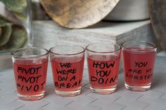 four shot glasses with words written on them sitting on a table next to a potted plant