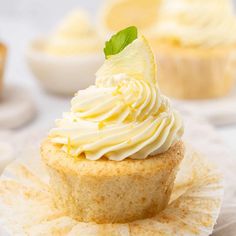 a cupcake with white frosting and a green leaf on top sits on a plate