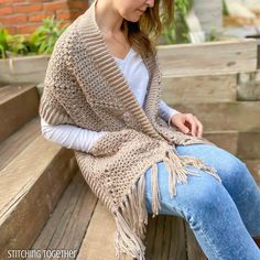 a woman sitting on top of a wooden bench wearing a knitted cardigan and jeans