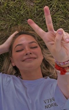 a woman laying in the grass making a peace sign with her hand and wearing a red bracelet