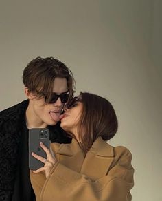 a man and woman kissing while holding a cell phone