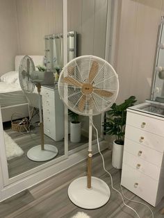 a white fan sitting on top of a wooden floor next to a dresser and mirror