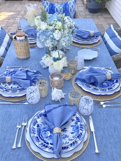 a table set with blue and white plates, napkins, silverware and flowers