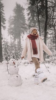 a woman walking in the snow next to a snowman with her arms outstretched and legs crossed