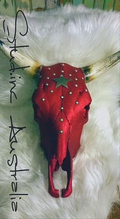 a red cow skull with horns and stars on it's head sitting on a white fur rug