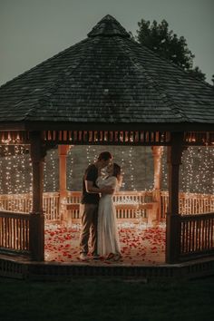 a bride and groom standing in front of a gazebo at night with lights on it