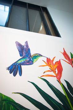 a painting of a hummingbird and flowers on a white background with green leaves in the foreground