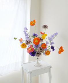 an arrangement of colorful flowers in a vase on a small table next to a window