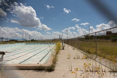 an empty swimming pool in the middle of a fenced off area with yellow flowers