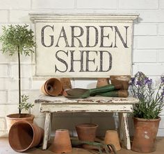 a garden shed sign surrounded by potted plants and gardening tools on a wooden table