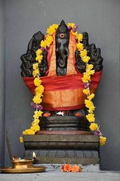 a statue with flowers around it and a candle on the ground in front of it