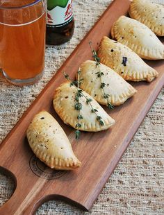 four pastries on a wooden tray next to a glass of beer and a bottle