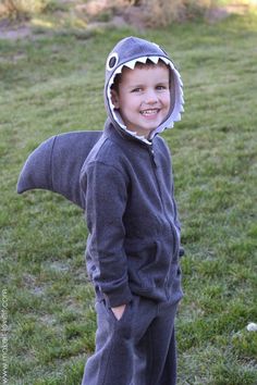 a young boy wearing a shark costume standing in the grass with his mouth wide open