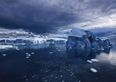 an iceberg floating in the ocean with dark clouds above it and blue water below