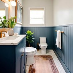 a white toilet sitting next to a bathroom sink under a mirror on top of a wooden cabinet