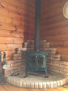 a wood burning stove sitting inside of a wooden room next to brick steps and a fan