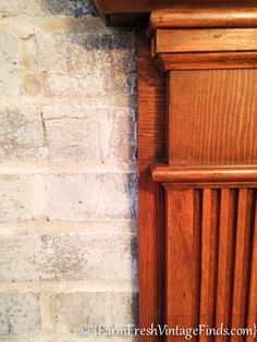 the corner of a wooden cabinet next to a brick wall with a clock on it