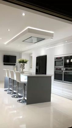 a large kitchen with white cabinets and counter tops, lights on the ceiling, and an island in the middle