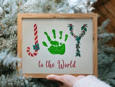 a handprinted christmas ornament is displayed in front of a pine tree