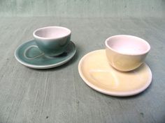 two cups and saucers sitting on top of a table next to eachother