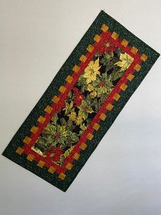 a quilted table runner with leaves and flowers on the border is hanging from a white wall