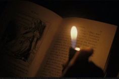 an open book with a lit candle in the middle and a hand holding it up