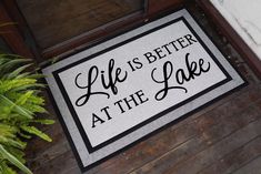 a door mat that says life is better at the lake on it next to a potted plant