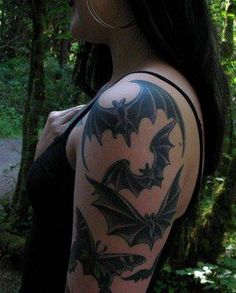 a woman with a bat tattoo on her arm and shoulder, standing in the woods