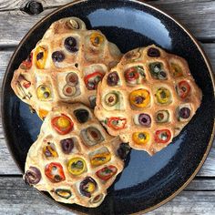 two waffles on a black plate with peppers and olives cut in half