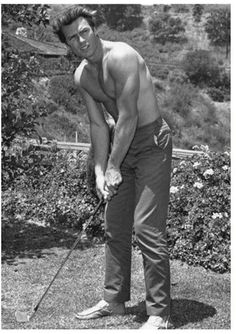 a shirtless man holding a golf club in his right hand and posing for the camera