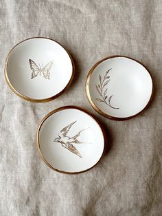 three white and gold plates with designs on them sitting on a cloth covered tablecloth