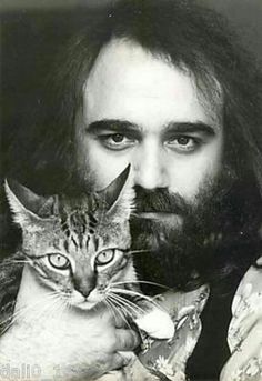 a man with long hair holding a cat in his arms and looking at the camera