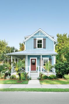 a blue house with red front door and shutters on the windows is surrounded by greenery