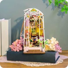 a doll house is sitting on top of a book shelf with flowers in front of it