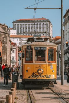 a yellow trolley car traveling down tracks next to tall buildings and people walking on the sidewalk